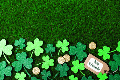 Flat lay composition with clover leaves and gold coins on green grass, space for text. St. Patrick's Day celebration