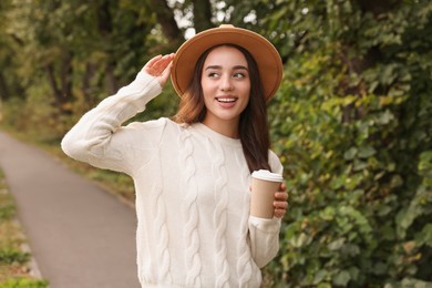 Photo of Beautiful young woman in stylish warm sweater holding paper cup of coffee outdoors
