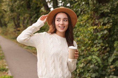 Beautiful young woman in stylish warm sweater holding paper cup of coffee outdoors