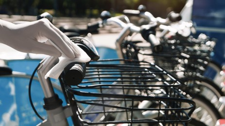 Photo of Woman in latex gloves cleaning bicycle handlebar with wet wipe outdoors, closeup. Protective measures