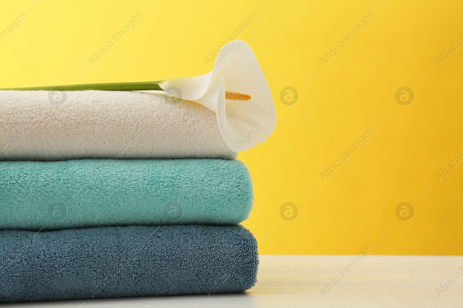 Photo of Stack of soft clean towels with beautiful flower on table against color background. Space for text