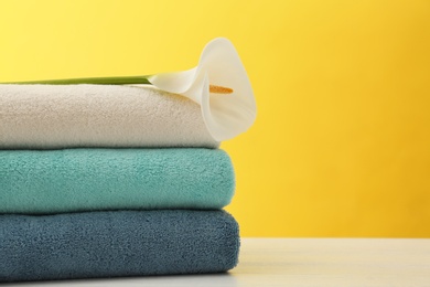 Stack of soft clean towels with beautiful flower on table against color background. Space for text