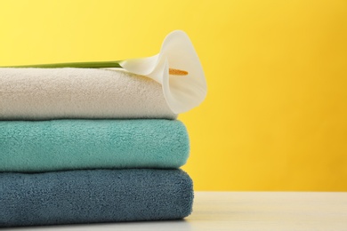 Photo of Stack of soft clean towels with beautiful flower on table against color background. Space for text