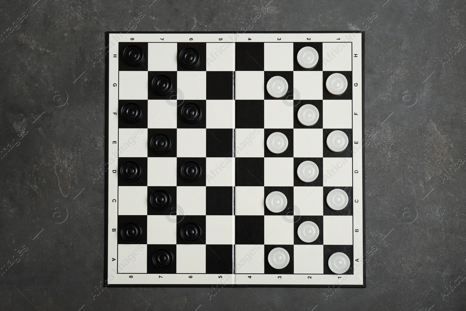 Photo of Checkerboard with game pieces on grey table, top view