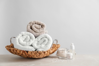 Photo of Basket with clean towels and cosmetic products on table against light background