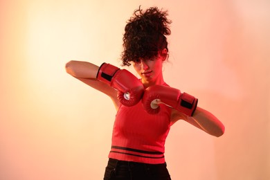 Beautiful young woman with boxing gloves on color background in neon lights