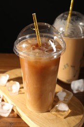 Photo of Refreshing iced coffee with milk in takeaway cups on table against black background, closeup