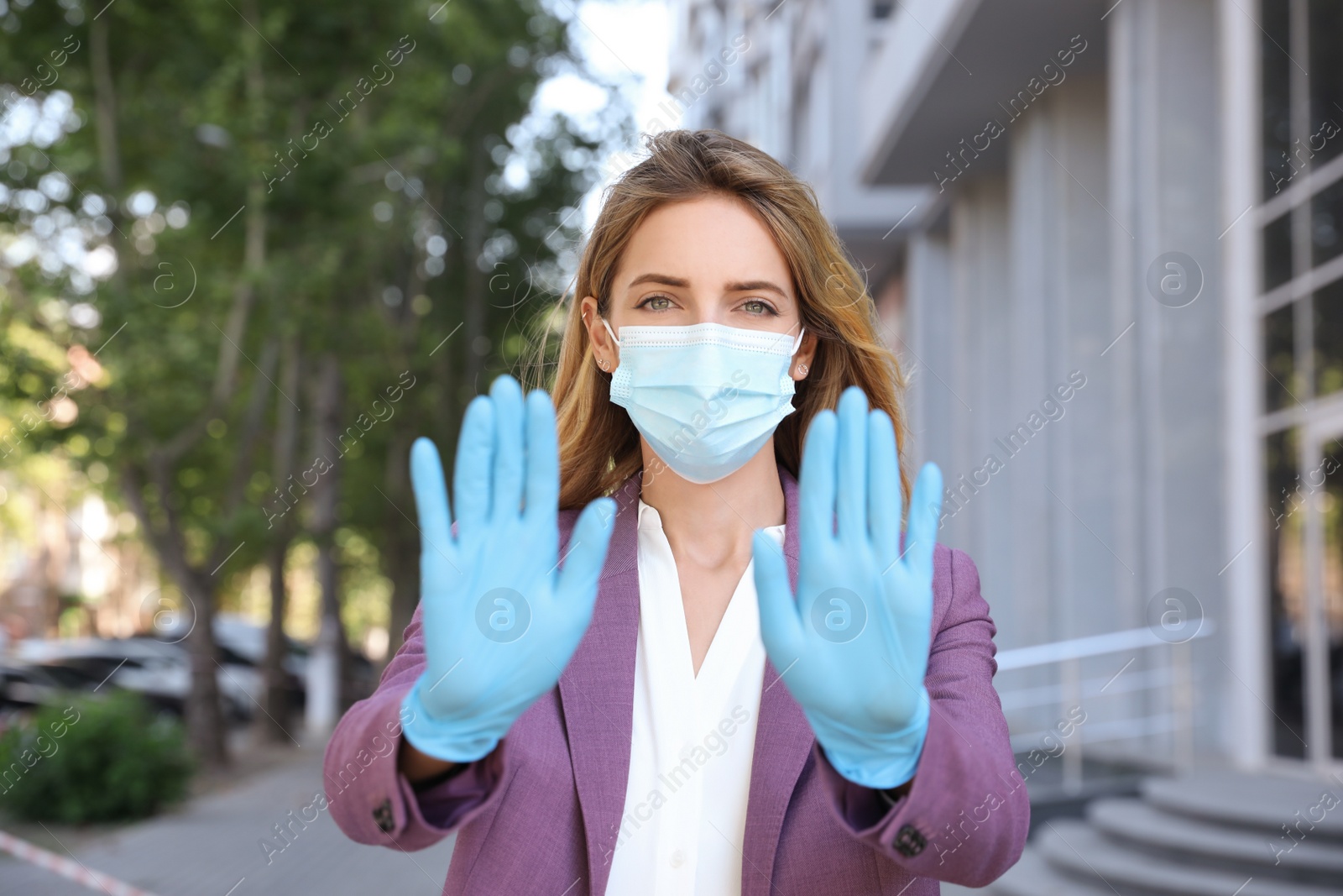 Photo of Woman in protective face mask showing stop gesture outdoors. Prevent spreading of coronavirus