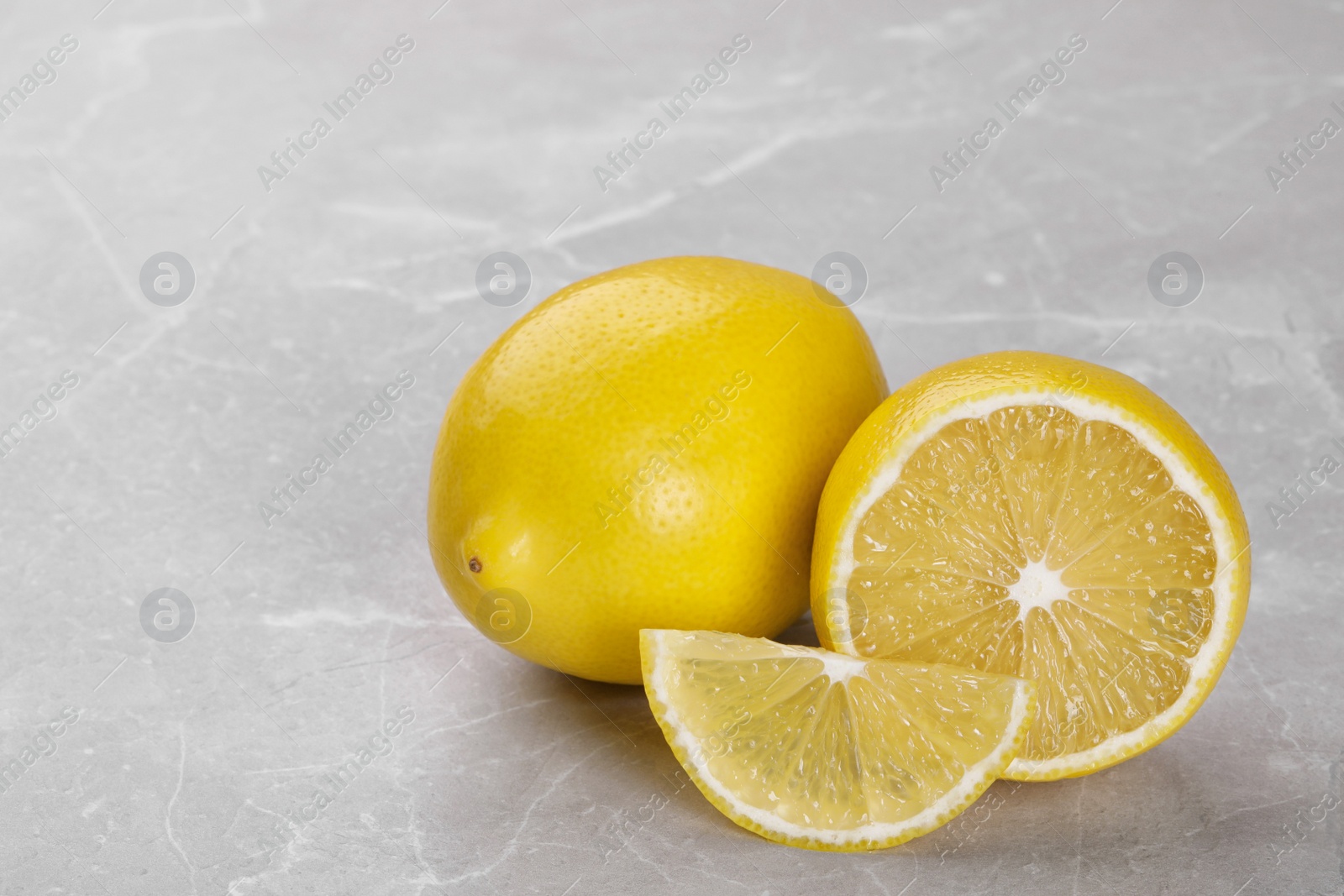 Photo of Whole and cut fresh ripe lemons on grey marble table