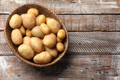 Raw fresh potatoes in wicker basket on wooden table, top view. Space for text