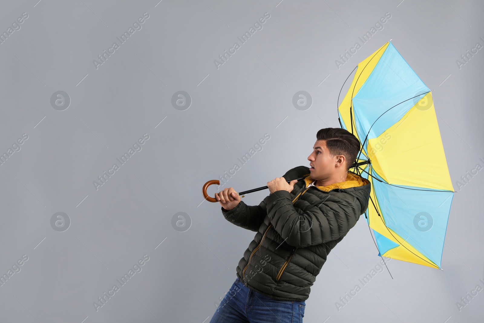 Photo of Emotional man with umbrella caught in gust of wind on grey background