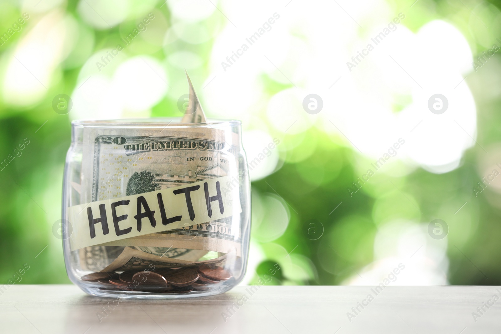 Photo of Glass jar with money and label HEALTH on table against blurred background. Space for text