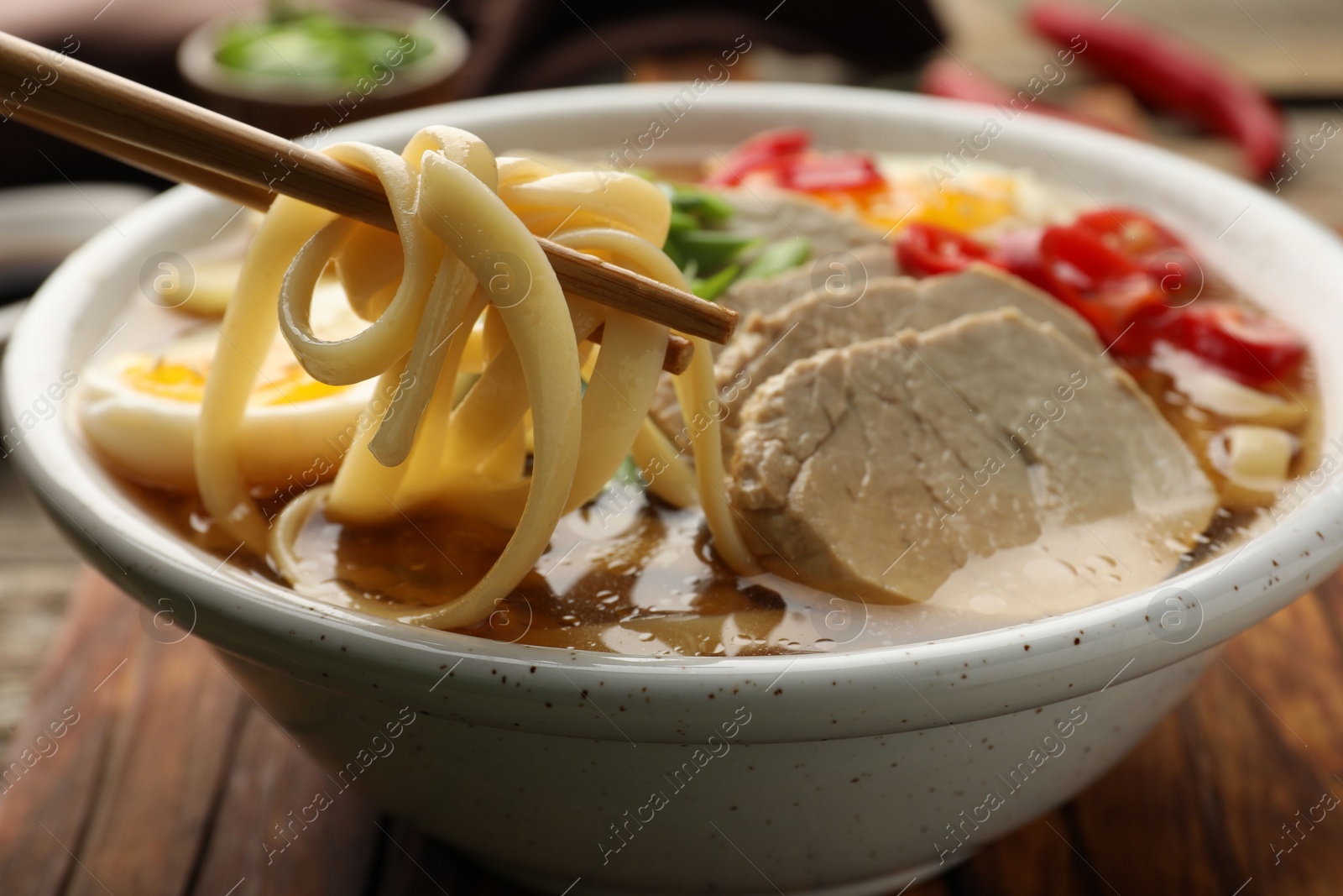 Photo of Eating delicious ramen with chopsticks at table, closeup. Noodle soup