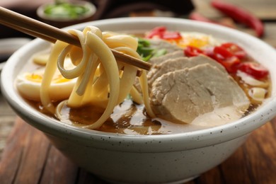 Photo of Eating delicious ramen with chopsticks at table, closeup. Noodle soup