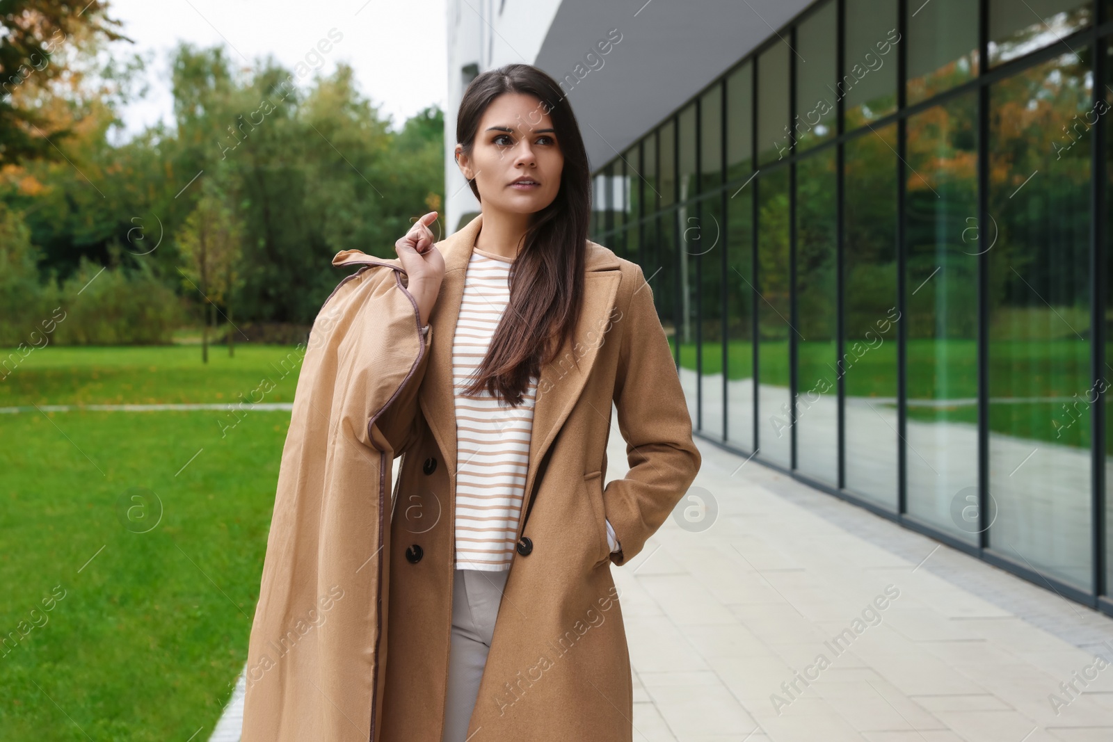 Photo of Attractive serious woman holding garment cover with clothes outdoors. Dry cleaning service