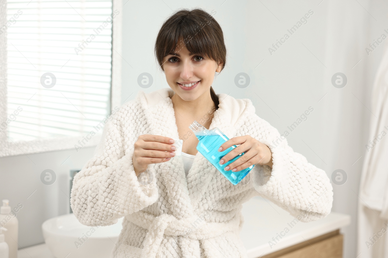 Photo of Young woman using mouthwash in bathroom. Oral hygiene