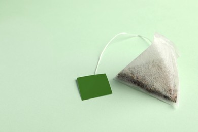 Photo of New tea bag with tab on light green background, closeup. Space for text