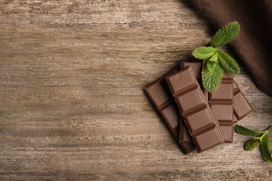 Photo of Tasty milk chocolate pieces with mint on wooden table, flat lay. Space for text