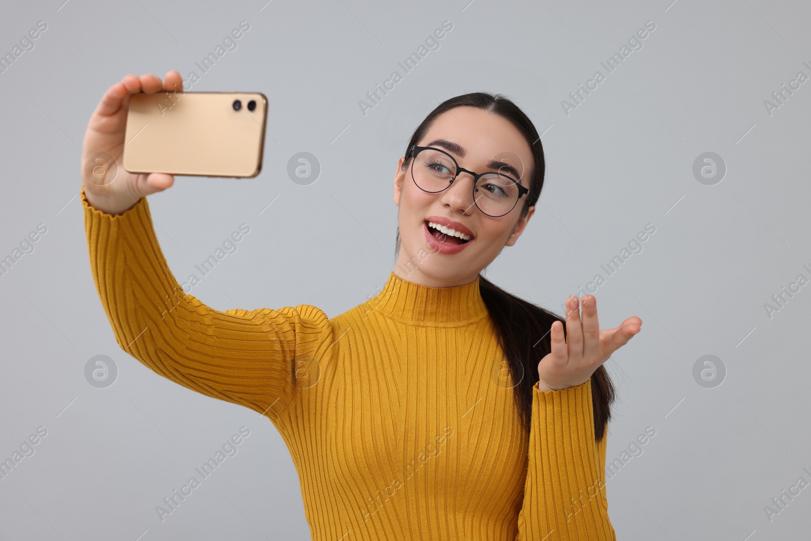 Photo of Smiling young woman taking selfie with smartphone on grey background