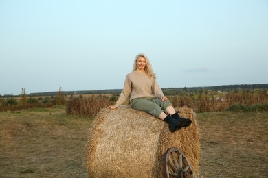 Beautiful woman sitting on hay bale in field. Autumn season
