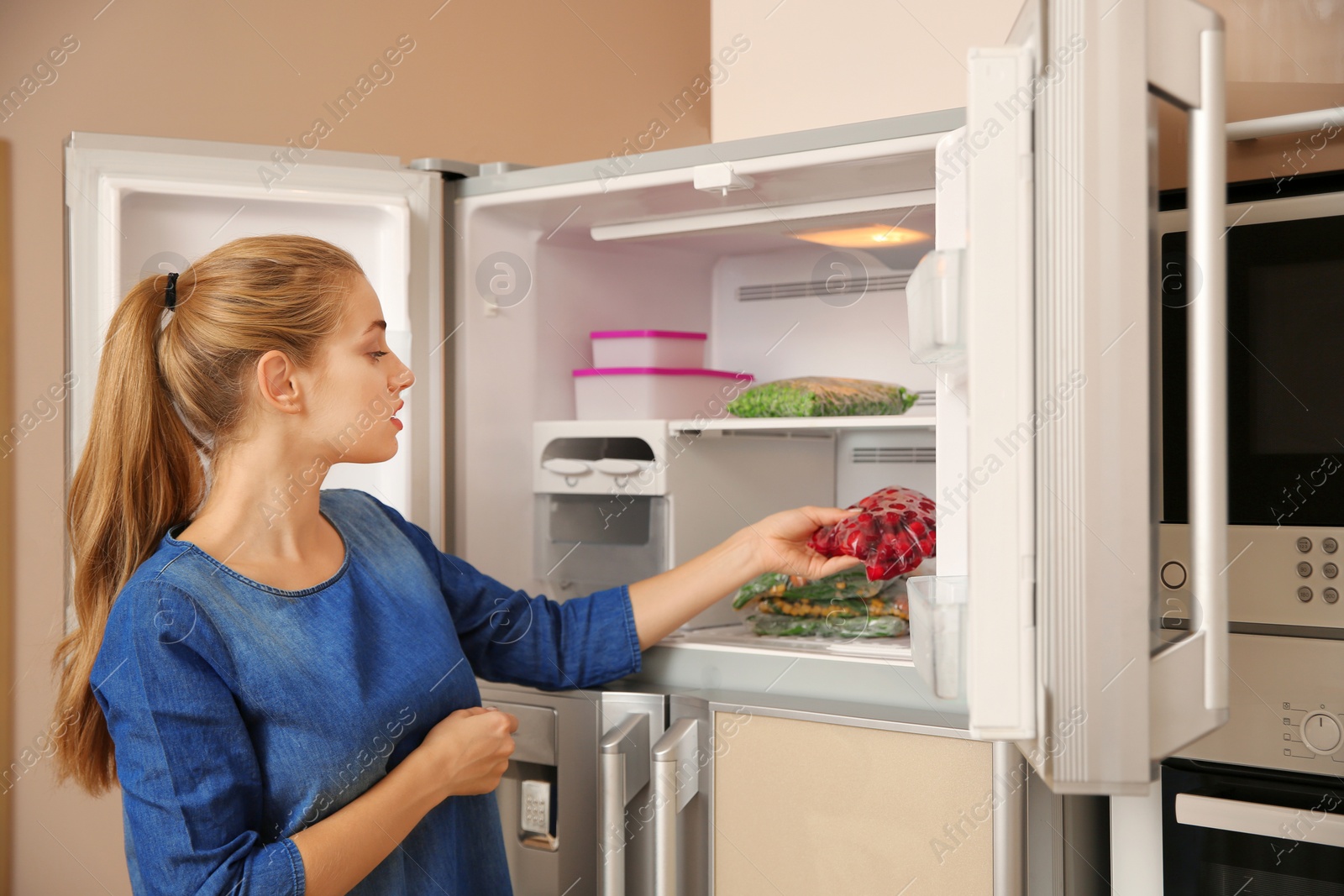 Photo of Young woman with frozen cherries near open refrigerator at home