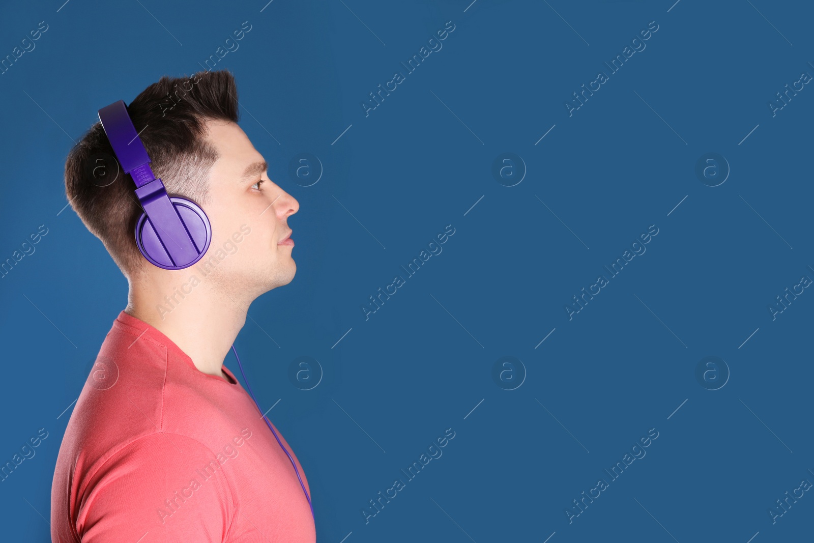 Photo of Man enjoying music in headphones on color background. Space for text