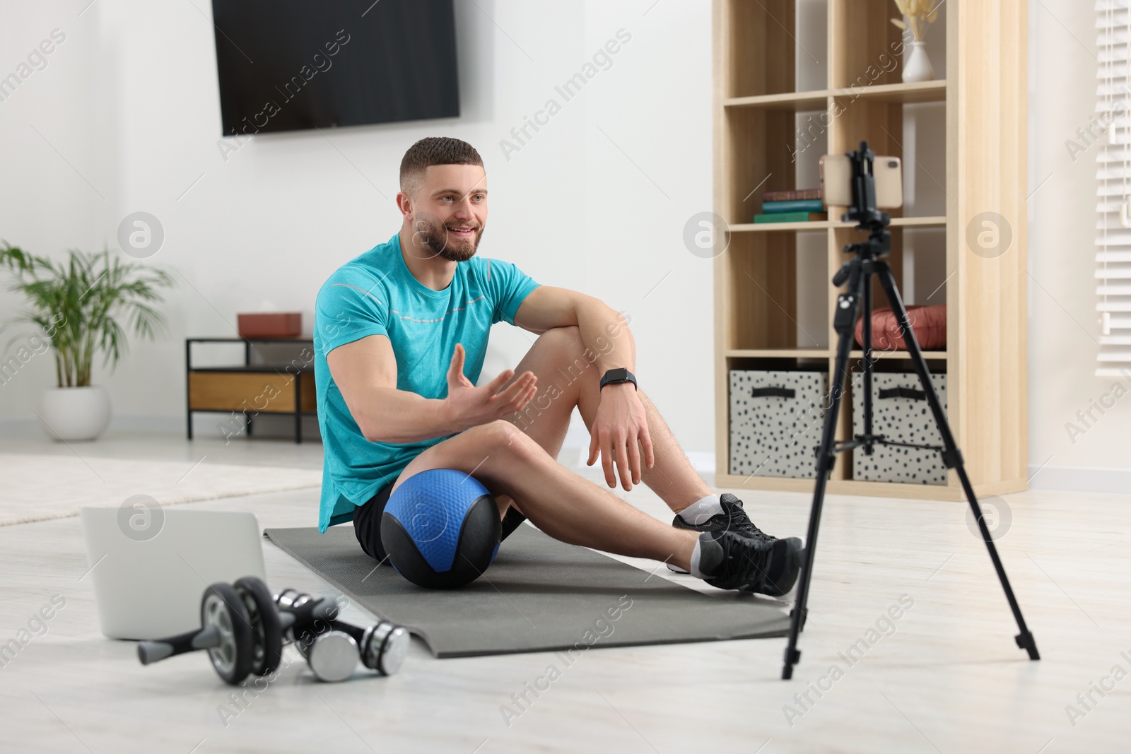 Photo of Trainer with ball streaming online fitness lesson on phone at home