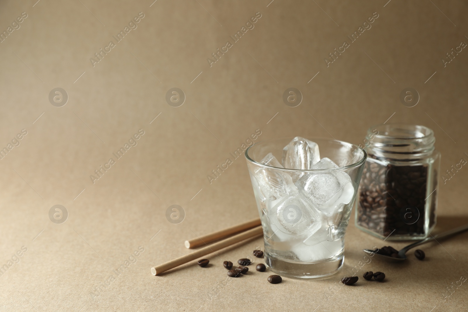 Photo of Cooking iced coffee. Ice cubes in glass, beans and straws on beige background. Space for text