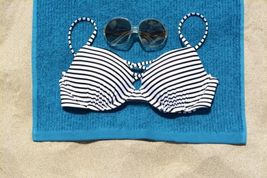 Photo of Blue beach towel, sunglasses and swimsuit on sand, top view