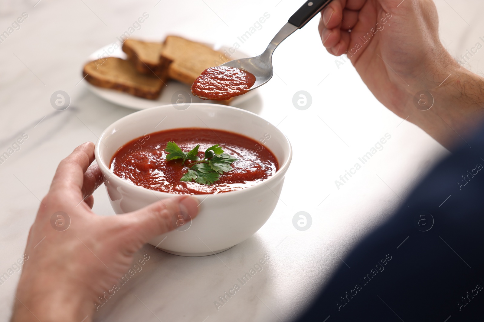 Photo of Man eating delicious tomato soup at light marble table, closeup