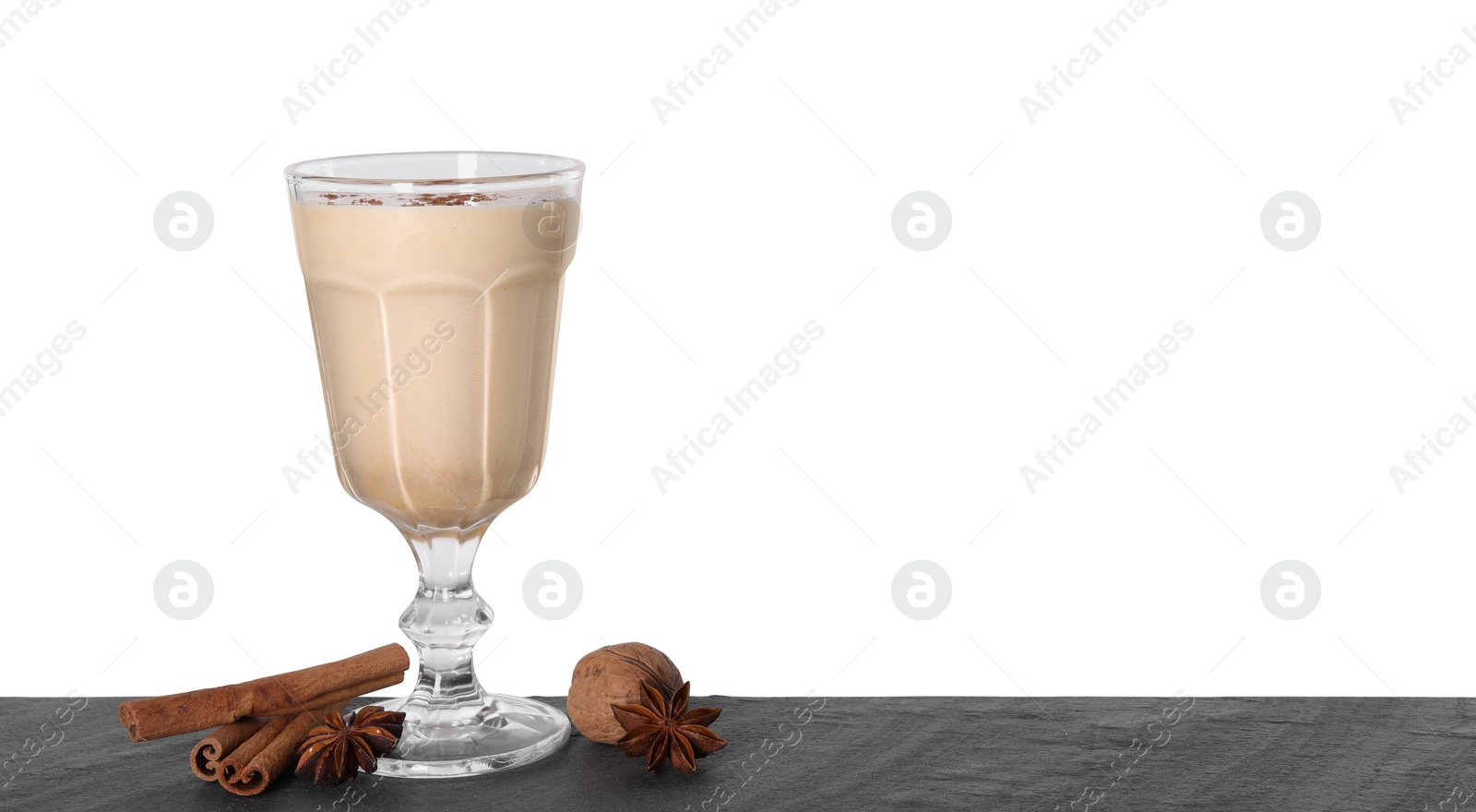 Photo of Delicious eggnog in glass, walnut and spices on grey table against white background, space for text