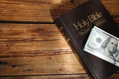 Holy Bible and money on wooden table, space for text