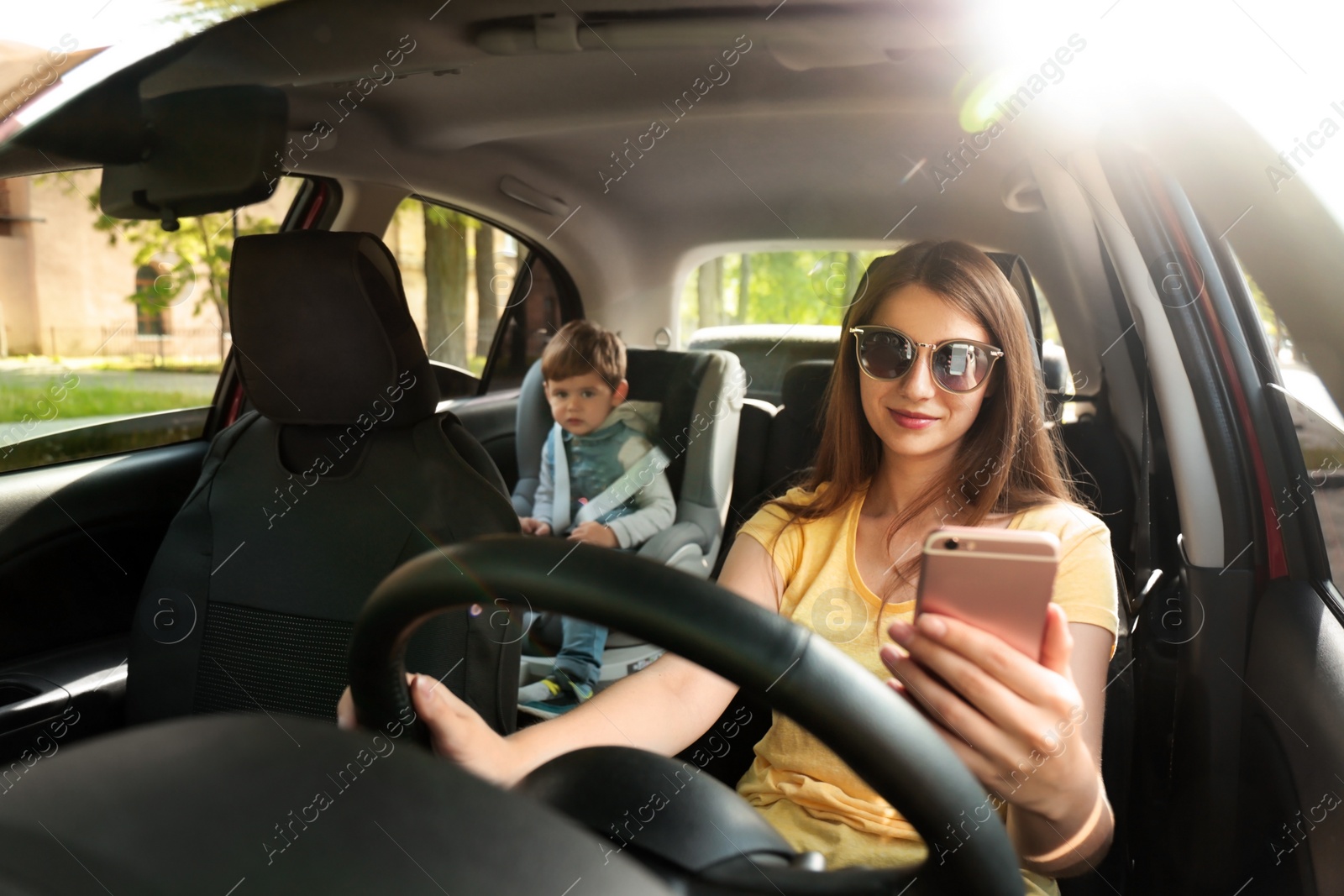 Photo of Mother using phone while driving car with her son on backseat. Child in danger