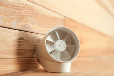 Photo of Portable fan on table near wooden wall. Summer heat