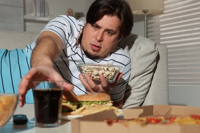 Photo of Overweight man with bowl of popcorn and drink on sofa at home