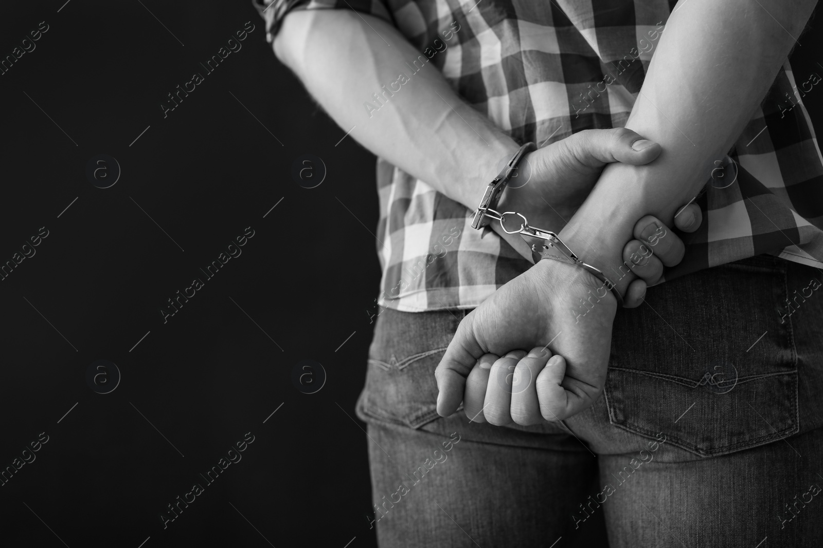 Photo of Criminal detained in handcuffs against dark background, space for text. Black and white effect