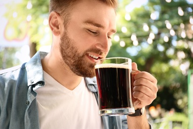 Photo of Handsome man with cold kvass outdoors, closeup. Traditional Russian summer drink