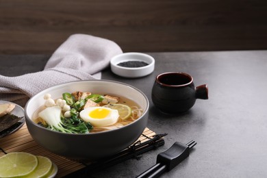 Photo of Bowl of vegetarian ramen served on grey table, space for text