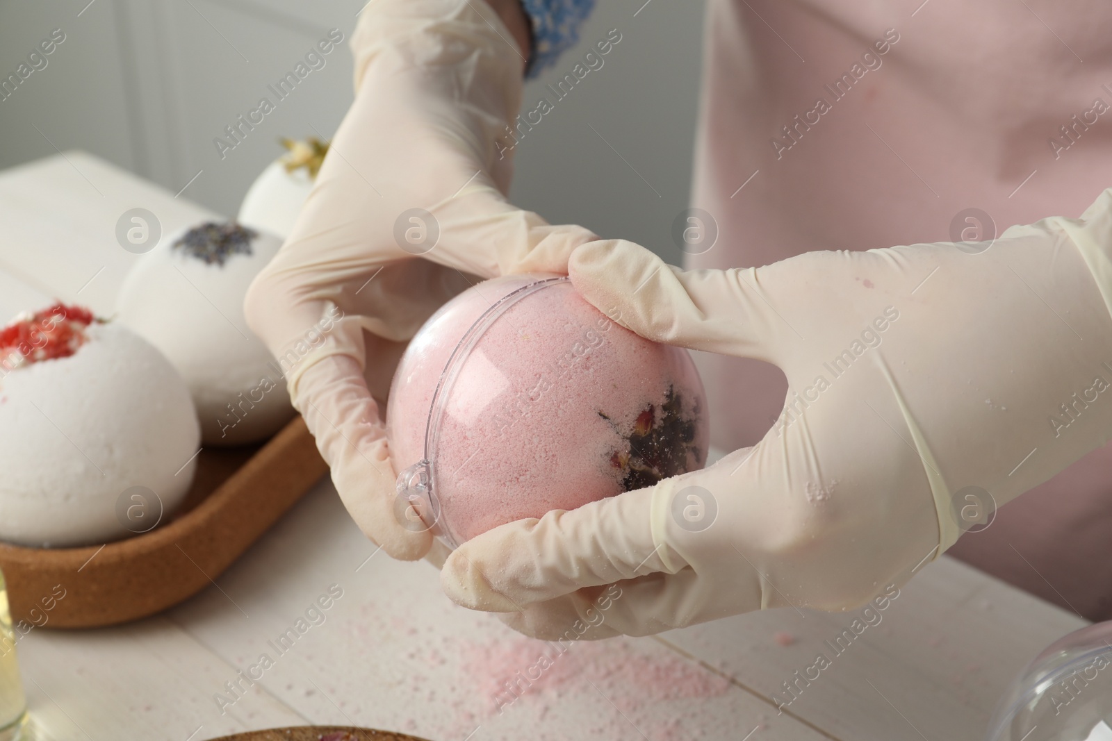 Photo of Woman in gloves making bath bomb at white table , closeup