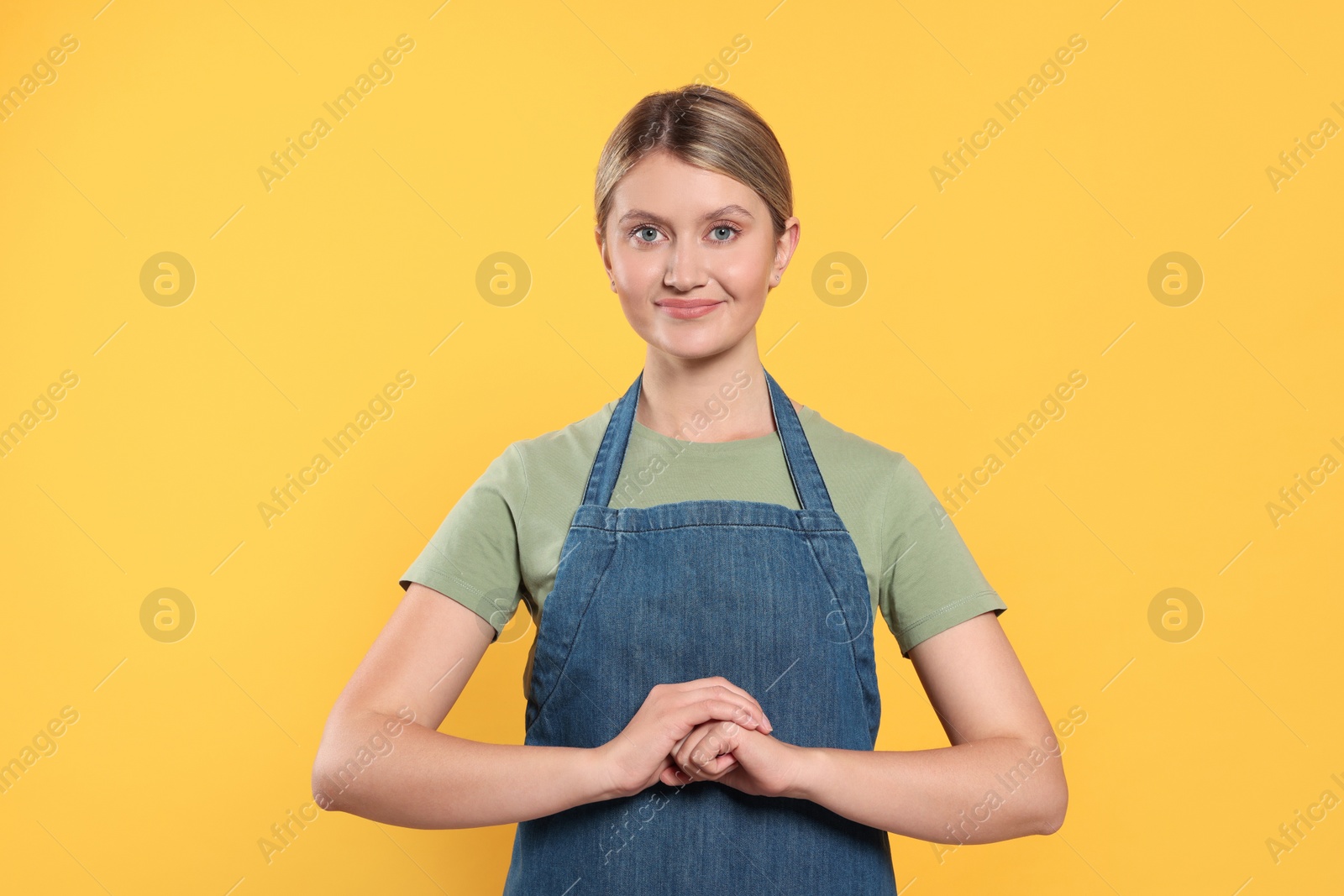 Photo of Beautiful young woman in denim apron on orange background