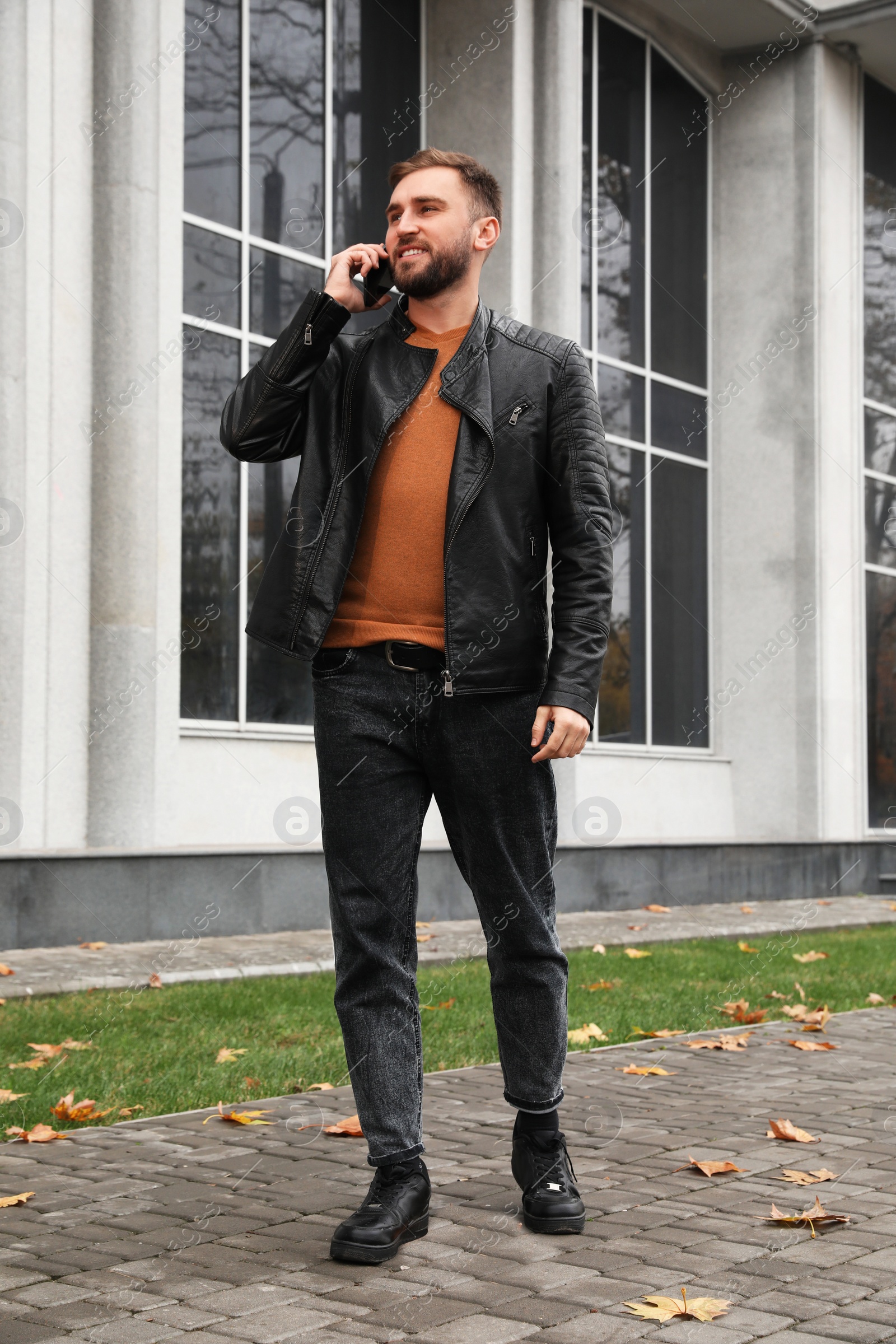 Photo of Handsome man in stylish leather jacket talking on mobile phone outdoors