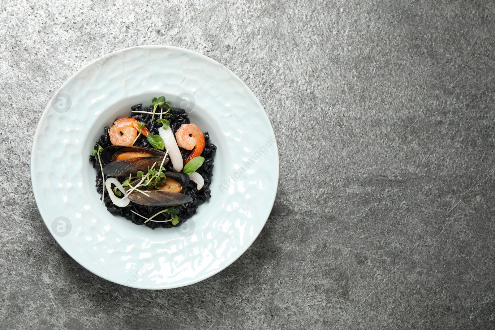 Photo of Delicious black risotto with seafood on grey table, top view. Space for text