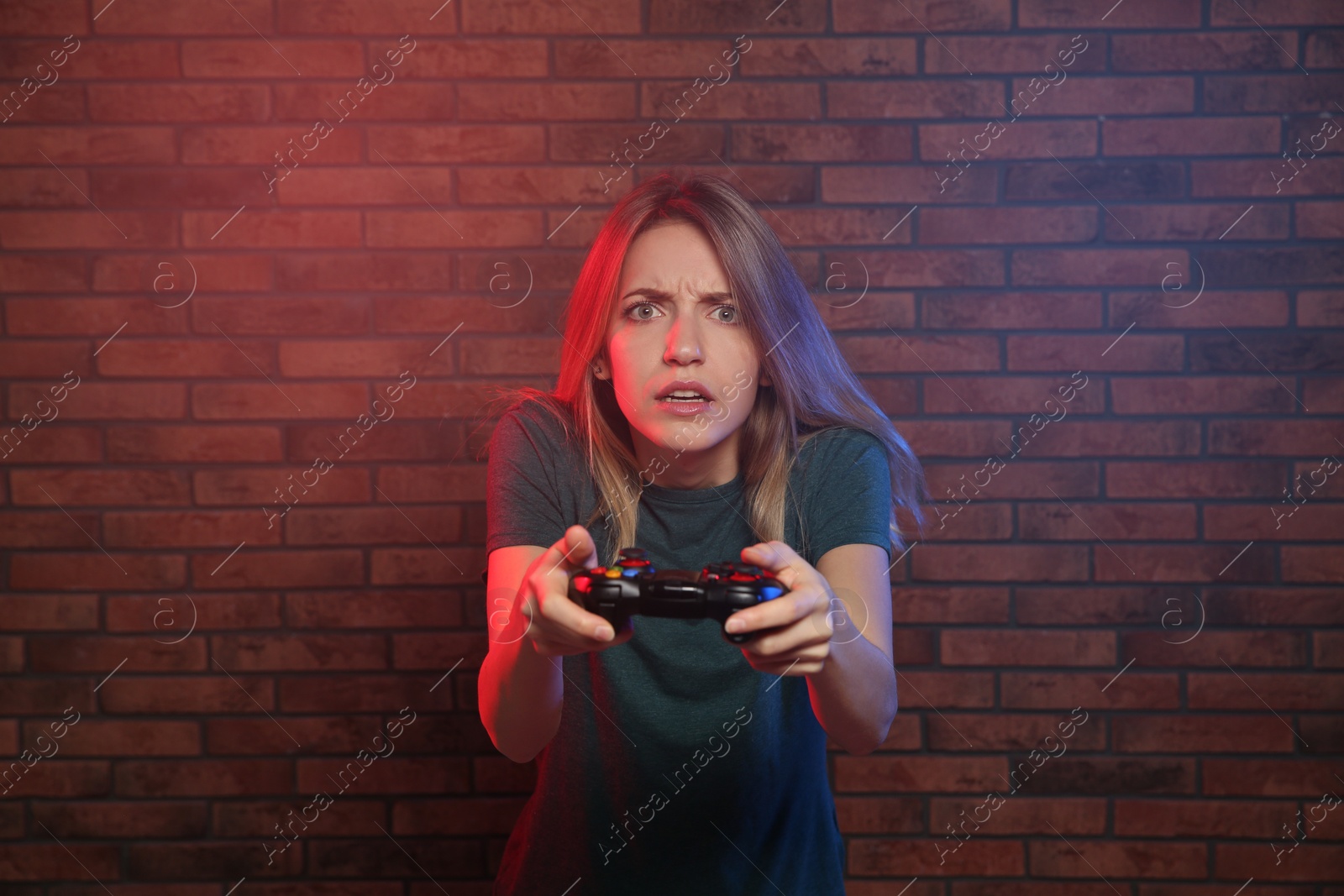 Photo of Emotional young woman playing video games with controller near brick wall