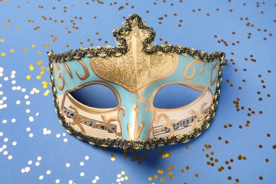 Photo of Beautiful carnival mask and shiny confetti on blue background, top view