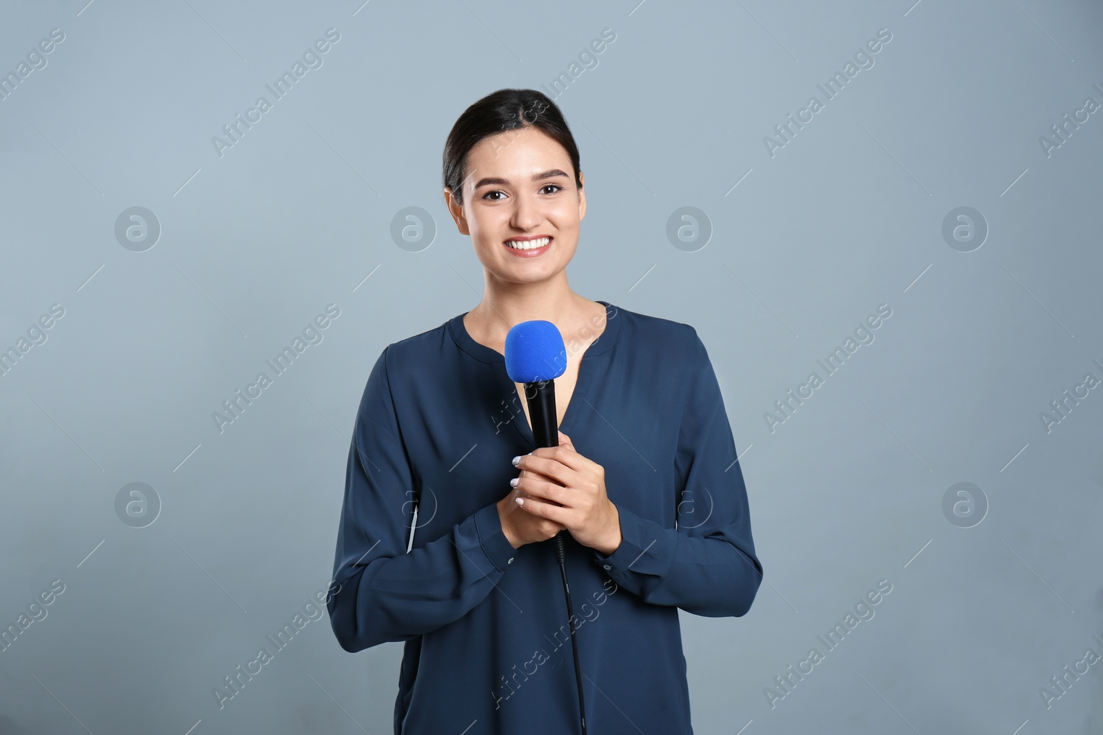 Photo of Young female journalist with microphone on grey background