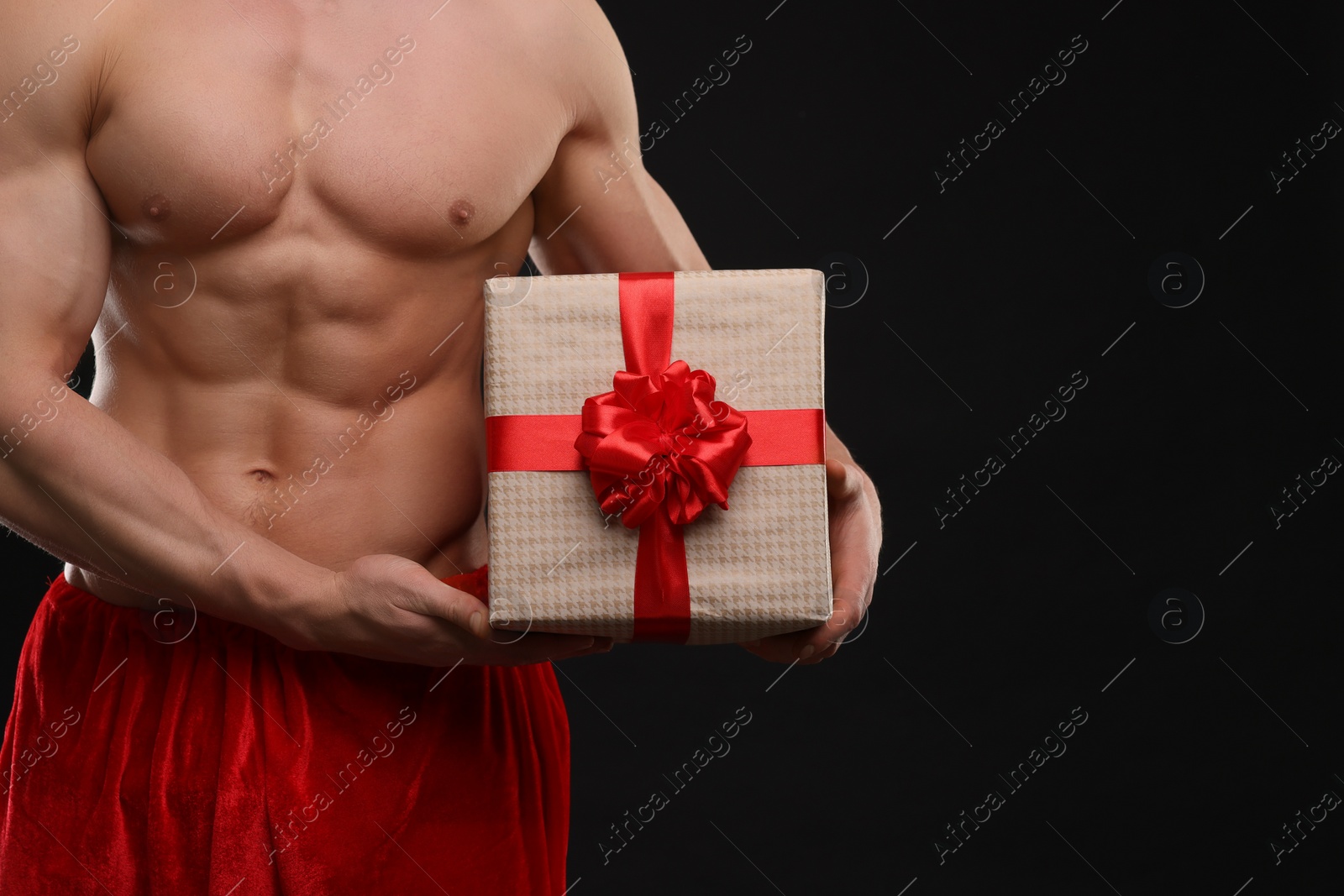 Photo of Attractive young man with muscular body holding Christmas gift box on black background, closeup. Space for text