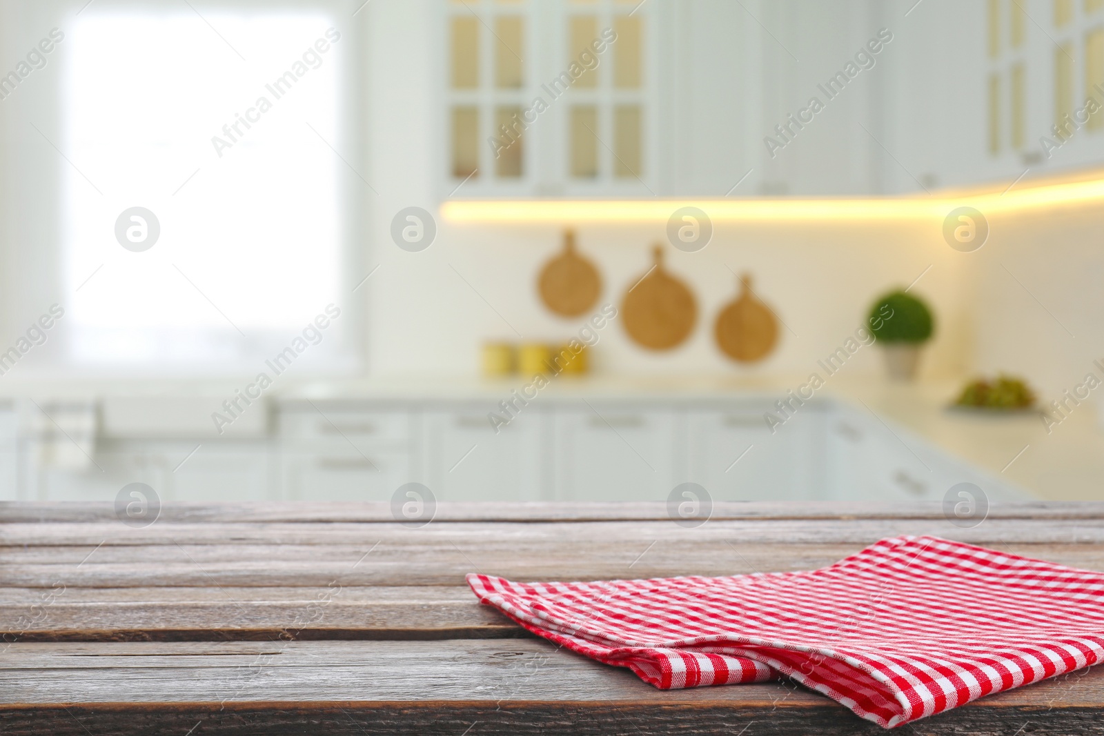 Image of Red checkered napkin on wooden table and blurred view of stylish kitchen interior. Space for design