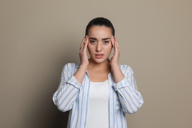 Photo of Young woman suffering from headache on beige background