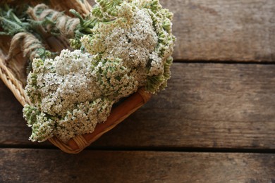 Photo of Basket with bunchesbeautiful dries yarrow on wooden table, top view. Space for text
