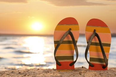 Photo of Stylish flip flops on sand near sea, space for text. Beach accessories